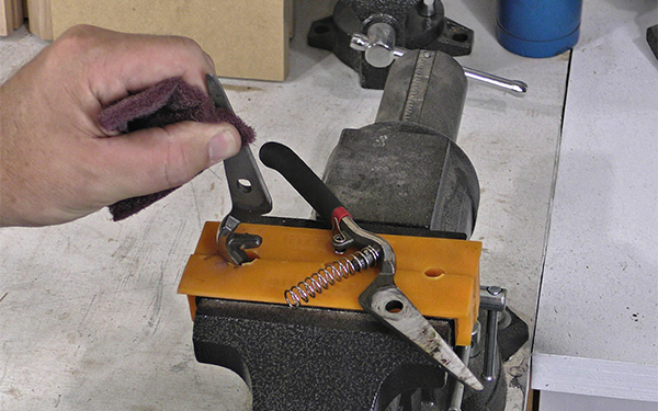A worker uses a non-woven abrasive pad to clean the blade of a small hand tool