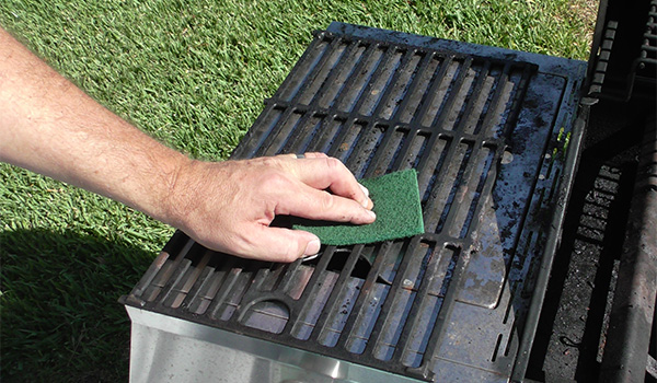 A worker uses a non-woven abrasive pad to clean a grill rack.