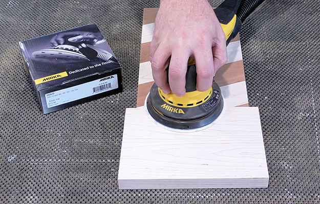 A person sands hardwood using a Mirka Gold sanding disc.