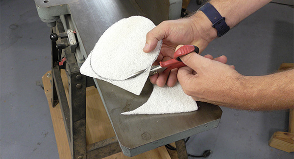 A woodworker cuts a non-woven pad to fit a random orbit sander