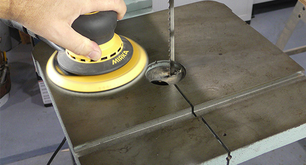 A worker sands the table of a bandsaw with a non-abrasive pad mounted to a random orbit sander.