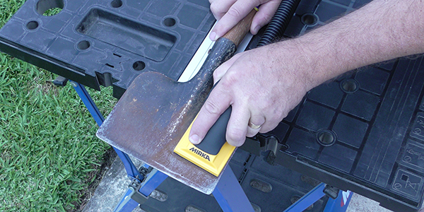 A gardener using a hand sander to remove rust from a garden tool