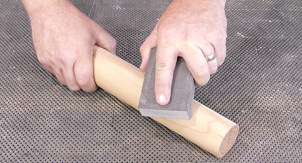A craftsperson uses a sanding sponge to sand the rounded face of a dowel