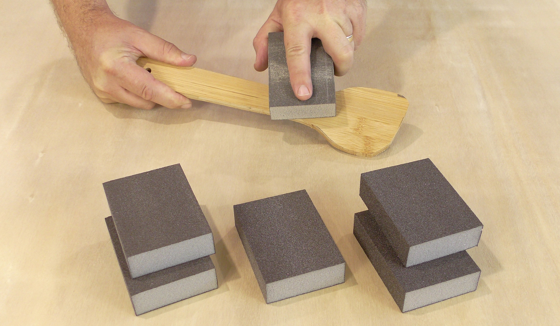 A craftsman uses a sanding sponge to sand a wooden spatula