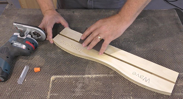 A craftsperson uses a sanding sponge to prep a template for use